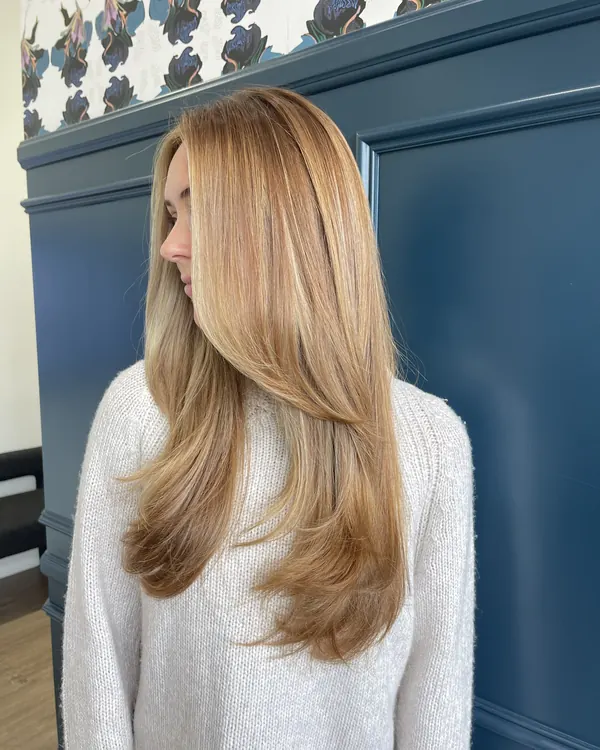 Strawberry blonde hair with face-framing layers and a smooth blowout by Aprille at Novum Hair Studio